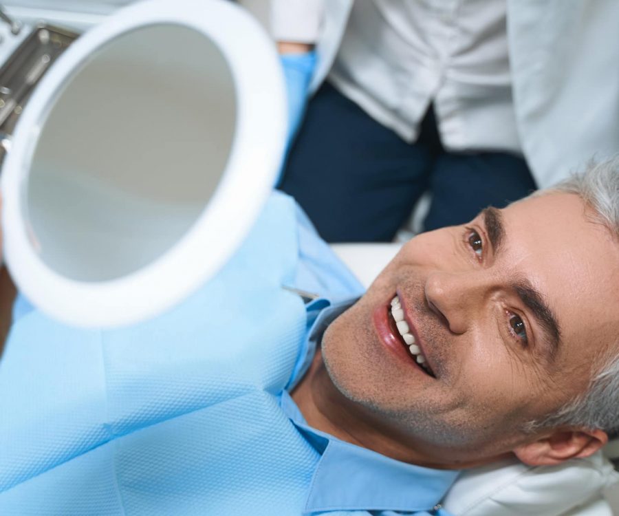 Joyful male is lying in chair and looking into mirror while being delighted with dentist work
